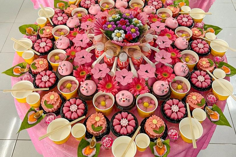 Mâm cúng đầy tháng bé gái tông hồng với 12 phần xôi chè nhỏ, gà luộc, giỏ trái cây và hoa đồng tiền