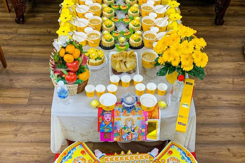 Mâm cúng đầy tháng bé trai tông vàng với xôi, chè, gà luộc, giỏ trái cây và bộ giấy cúng trên bàn phủ khăn ren trắng