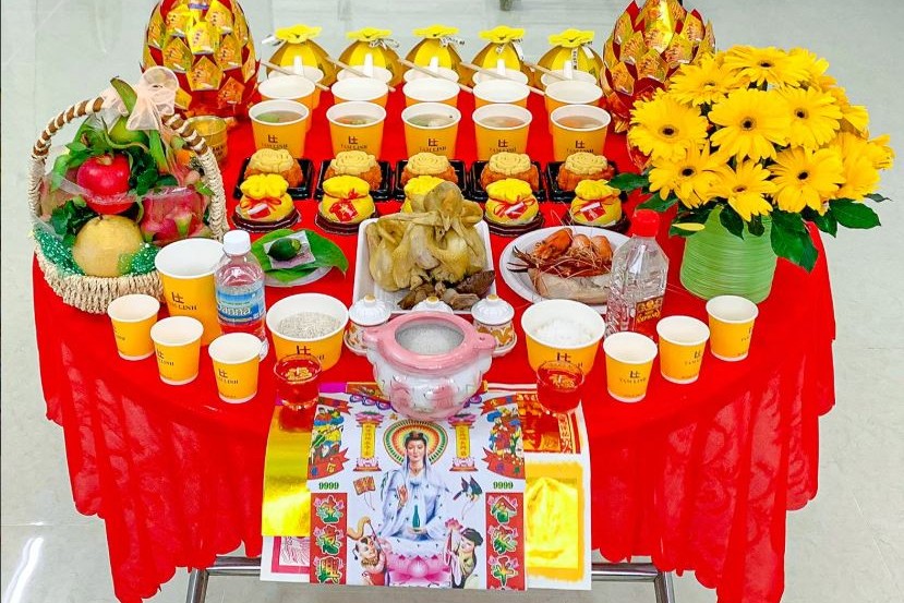 Mâm lễ gồm giỏ trái cây, hoa đồng tiền, xôi, chè, gà luộc và giấy cúng bày trên bàn tròn phủ khăn đỏ
