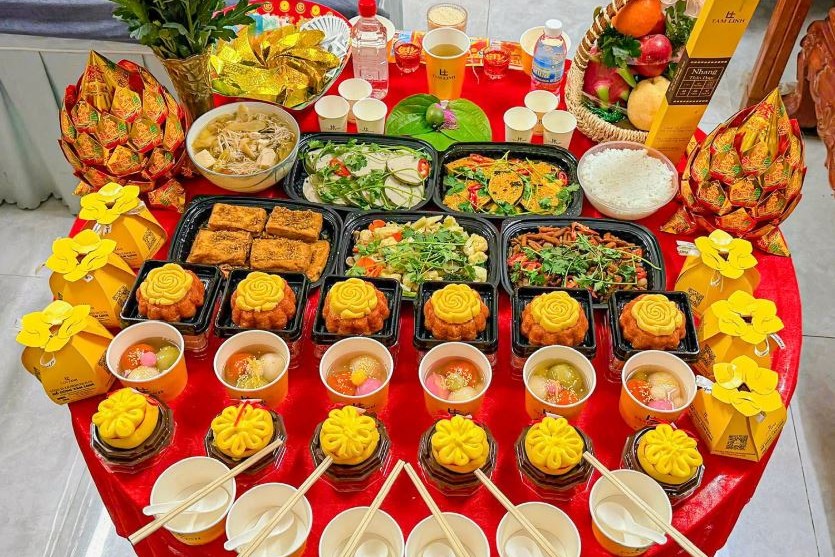 Mâm cúng chay với hoa cúc vàng, giỏ trái cây, xôi, chè và các món chay bày trên bàn tròn phủ khăn đỏ