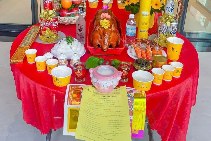 Mâm cúng đất đai với heo quay, tôm, trái cây, hoa đồng tiền, hũ gạo muối và giấy cúng trên bàn tròn phủ khăn đỏ