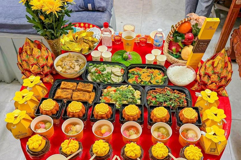 Mâm cúng với xôi, chè, trái cây, hoa cúc vàng và bánh kẹo bày trên bàn tròn phủ khăn đỏ