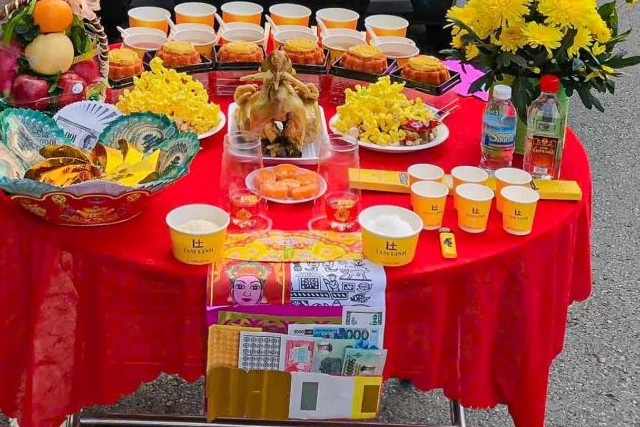 Mâm cúng xe mới với trái cây, xôi, chè, gà luộc và hoa cúc vàng bày trước đầu xe