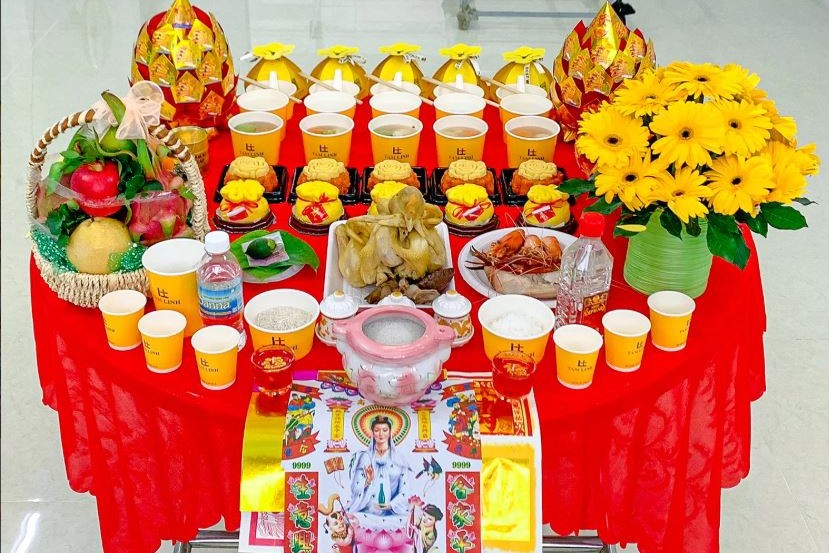 Mâm cúng giỗ tổ nghề may với gà luộc, bộ tam sên, trầu cau, xôi chè, trái cây và hoa trên bàn phủ khăn đỏ