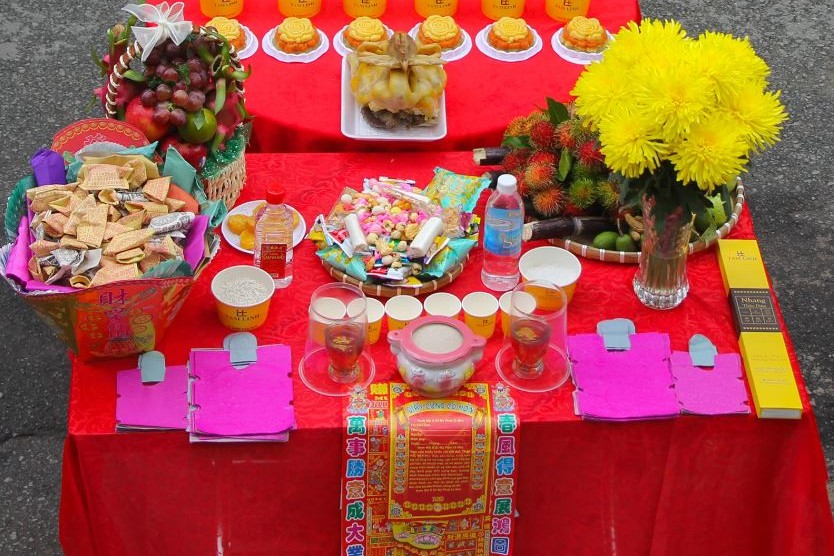 Giấy tiền, giấy áo và sớ cúng bày cùng bánh kẹo, hoa cúc vàng trên bàn lễ ngoài trời