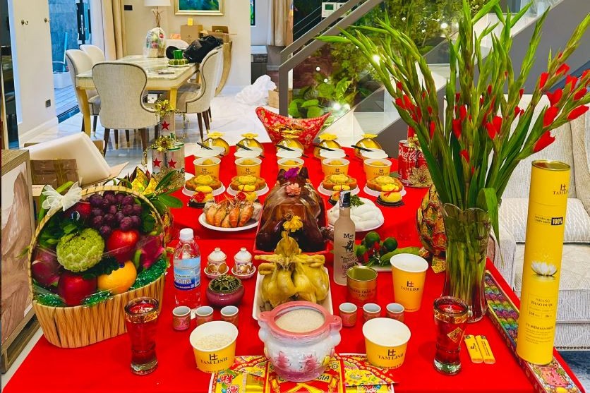 Mâm cúng về nhà mới với heo quay, gà luộc, giỏ trái cây, hoa lay ơn và giấy cúng bày trong phòng khách