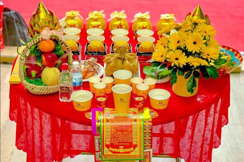 Mâm lễ với gà luộc, xôi, chè, giỏ trái cây và hoa đồng tiền vàng bày trên bàn phủ khăn đỏ