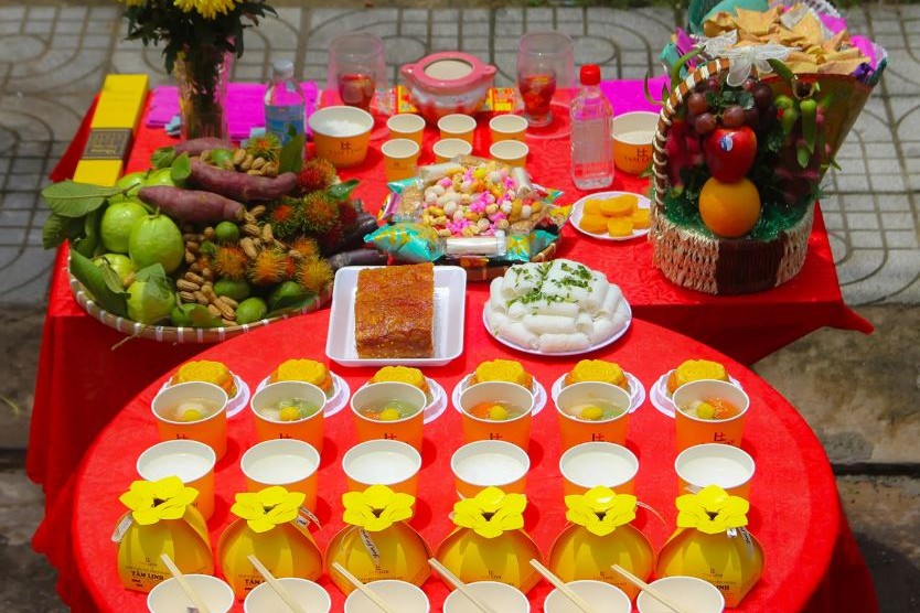 Mâm cúng cô hồn bày ngoài trời với heo quay, bánh hỏi, trái cây, bánh kẹo, cháo trắng và hoa cúc vàng